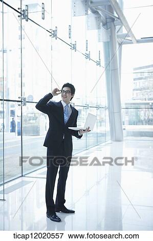 Stock Photo - a business man standing with a laptop. Fotosearch