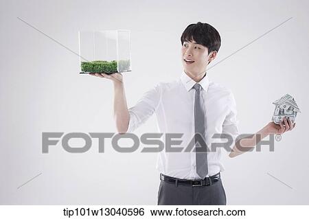 Stock Photograph - a business man with a transparent box of grass and a house of money. Fotosearch