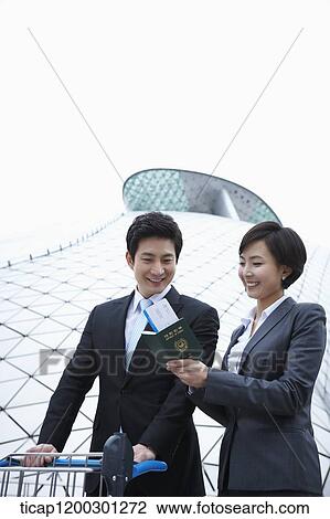 Stock Image - a businessman and businesswoman with baggage cart at the airport. Fotosearch