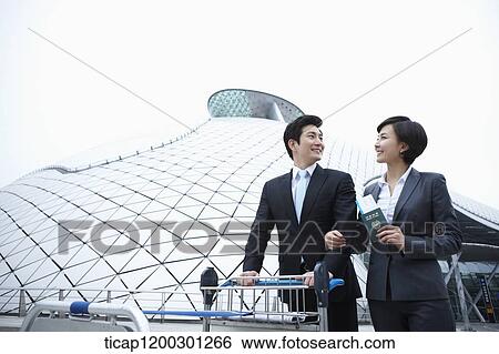Stock Photograph - a businessman and businesswoman with baggage cart at the airport. Fotosearch