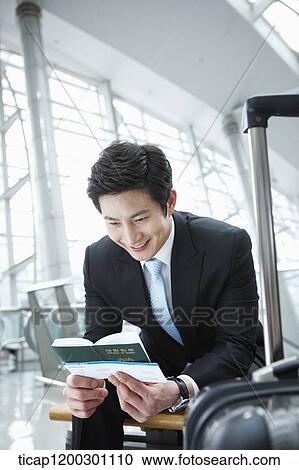 Stock Image - a businessman holding passport and boarding pass in the airport. Fotosearch
