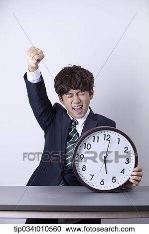 Stock Image - a businessman looking happy at desk with a clock. Fotosearch