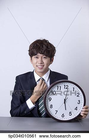 Stock Image - a businessman looking happy at desk with a clock. Fotosearch