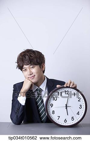 Stock Image - a businessman looking happy at desk with a clock. Fotosearch
