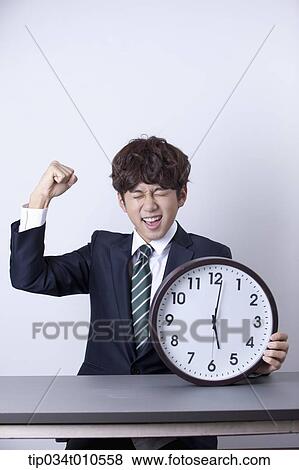 Stock Photo - a businessman looking happy at desk with a clock. Fotosearch
