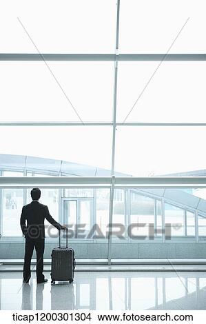 Picture - a businessman looking outside the window in the airport. Fotosearch