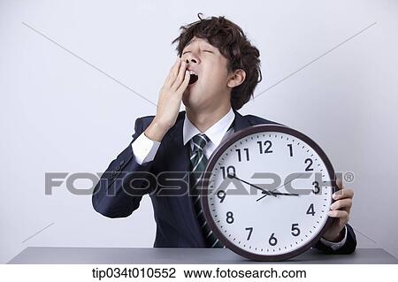 Stock Image - a businessman looking sleepy with a clock. Fotosearch