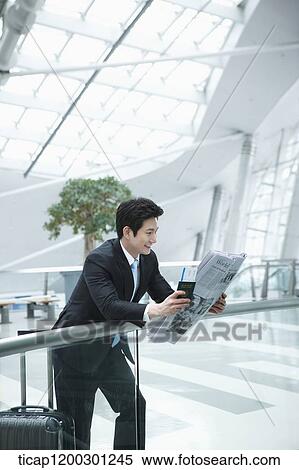 Stock Photography - a businessman reading a newspaper while leaning on fence in the airport. Fotosearch