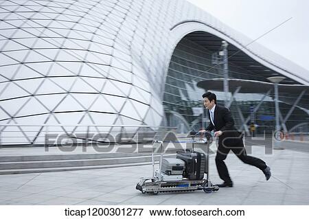 Stock Photo - a businessman running with baggage cart at the airport. Fotosearch