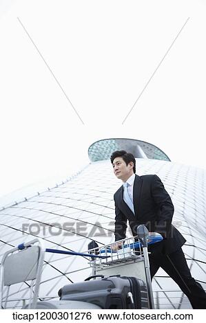Stock Photograph - a businessman running with baggage cart at the airport. Fotosearch