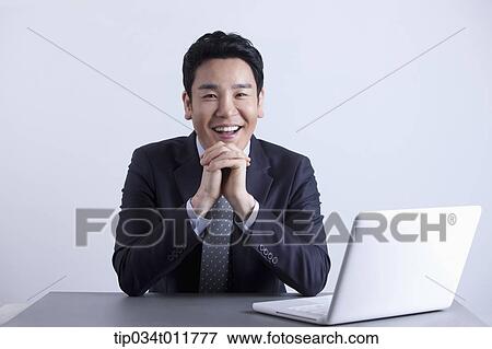 Stock Photo - a businessman smiling with a laptop on the desk. Fotosearch