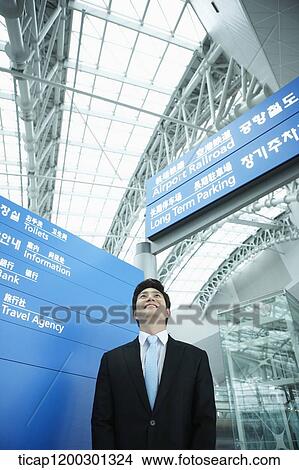 Picture - a businessman standing in front of a information board in the airport. Fotosearch
