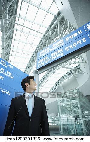 Stock Photograph - a businessman standing in front of a information board in the airport. Fotosearch