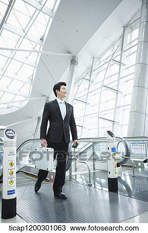 Stock Image - a businessman stepping out of escalator in the airport. Fotosearch