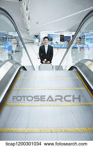 Picture - a businessman taking escalator in the airport. Fotosearch