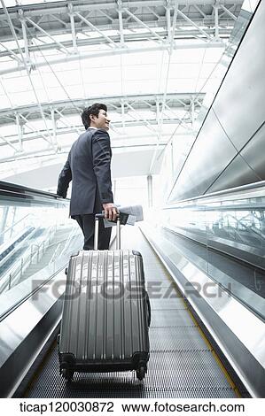 Stock Image - a businessman taking escalator in the airport. Fotosearch