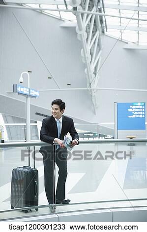 Stock Image - a businessman with suitcase leaning on fence in the airport. Fotosearch