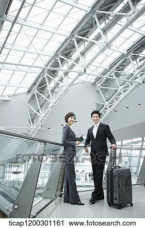 Stock Image - a businesswoman and businessman having a chat in the airport. Fotosearch