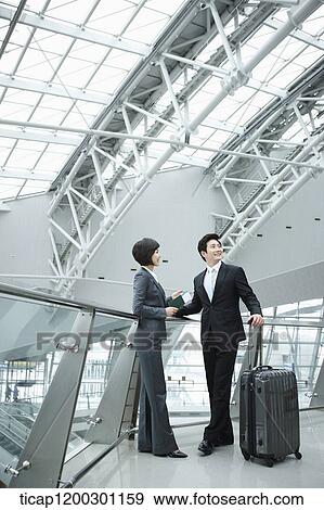 Stock Photo - a businesswoman and businessman having a chat in the airport. Fotosearch