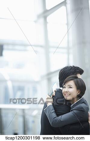 Stock Photo - a businesswoman and businessman hugging each other in the airport. Fotosearch