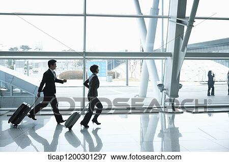 Stock Photo - a businesswoman and businessman running with suitcase in the airport. Fotosearch