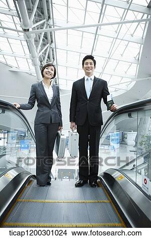 Picture - a businesswoman and businessman talking escalator in the airport. Fotosearch