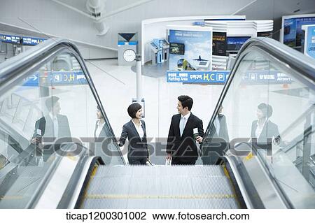 Stock Image - a businesswoman and businessman talking escalator in the airport. Fotosearch