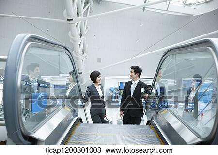 Stock Image - a businesswoman and businessman talking escalator in the airport. Fotosearch