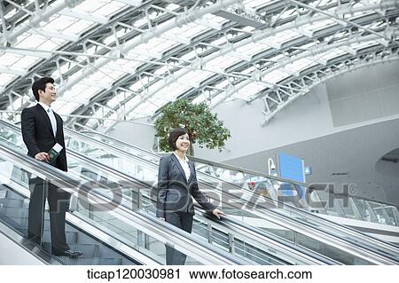 Stock Image - a businesswoman and businessman talking escalator in the airport. Fotosearch