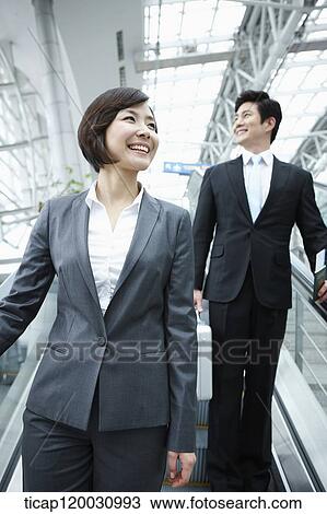 Stock Image - a businesswoman and businessman talking escalator in the airport. Fotosearch