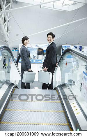 Stock Photo - a businesswoman and businessman talking escalator in the airport. Fotosearch