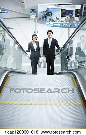 Stock Photo - a businesswoman and businessman talking escalator in the airport. Fotosearch