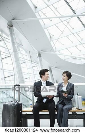 Picture - a businesswoman and businessman using laptop in the airport. Fotosearch