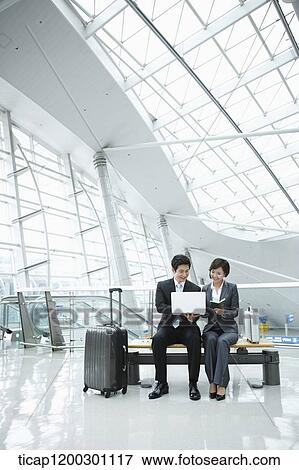Stock Photo - a businesswoman and businessman using laptop in the airport. Fotosearch