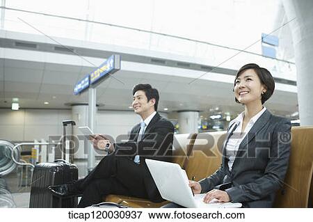 Stock Photo - a businesswoman and businessman using devices in the airport. Fotosearch