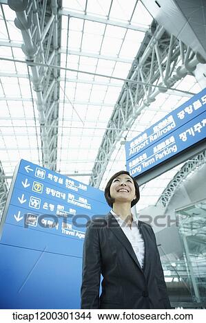Picture - a businesswoman standing in front of a information board in the airport. Fotosearch