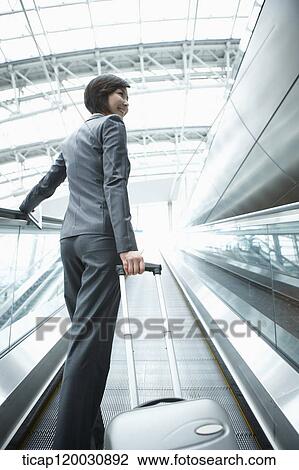 Stock Image - a businesswoman taking escalator in the airport. Fotosearch