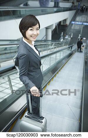 Stock Image - a businesswoman taking escalator in the airport. Fotosearch
