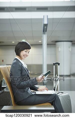 Stock Image - a businesswoman using laptop in the airport. Fotosearch