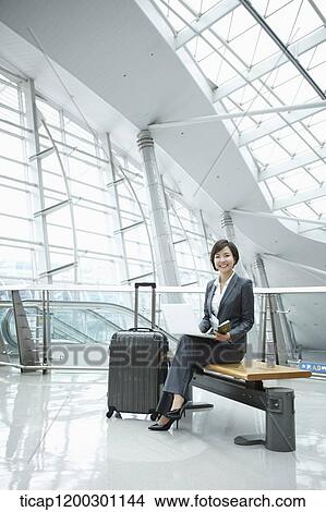 Picture - a businesswoman using laptop while sitting on a bench in the airport. Fotosearch