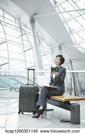 Stock Photo - a businesswoman using laptop while sitting on a bench in the airport. Fotosearch