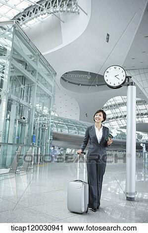 Stock Image - a businesswoman walking with a suitcase in the airport. Fotosearch