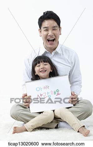 Stock Image - a daughter sitting in fathers lap and holding a notebook. Fotosearch