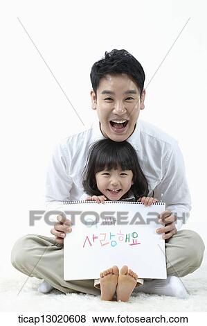 Stock Photo - a daughter sitting in fathers lap and holding a notebook. Fotosearch
