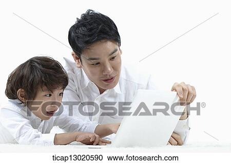 Stock Image - a father lying on the floor with his son while playing on laptop. Fotosearch