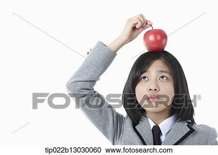 Stock Image - a girl in a school uniform and an apple on her head. Fotosearch