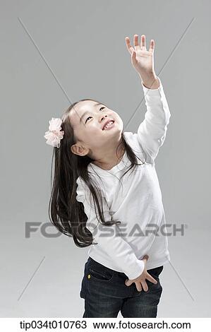 Stock Image - a girl in white shirt and jeans trying to reach something. Fotosearch