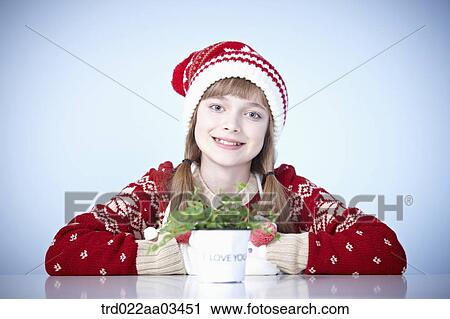 a girl in winter outfit sitting at table with a Christmas plant View Large Photo Image Stock Image - a girl in winter outfit sitting at table with a Christmas plant. Fotosearch