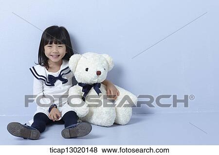 Stock Photo - a girl sitting next to a teddy bear. Fotosearch