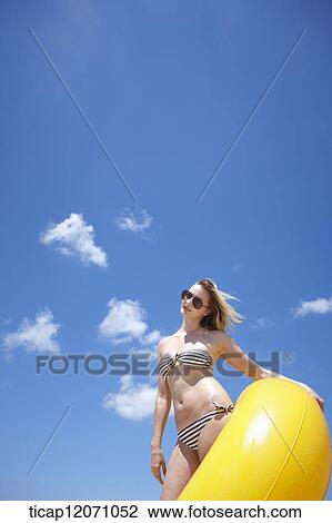 Stock Image - a lady in bikini and beach tube under bright sky. Fotosearch